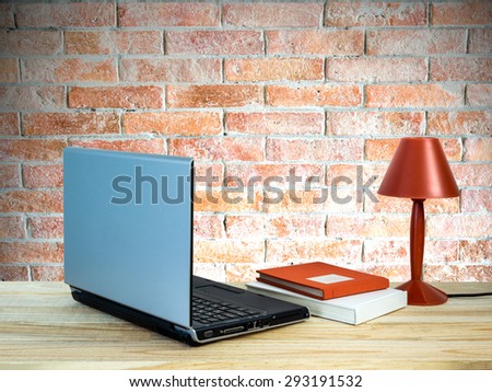 Red lamp with laptop computer, books on wooden table top over brick wall background/ interior still life