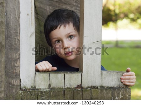 Portrait of a small child in a wooden window of a play house in a playground in a park or a garden.