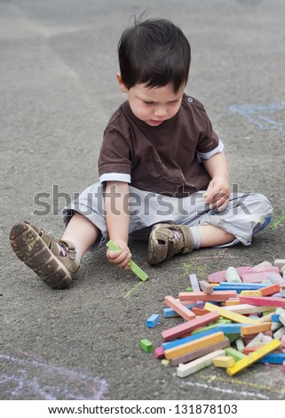 Small child, boy or girl, drawing on a asphalt road or pavement with a chalk.