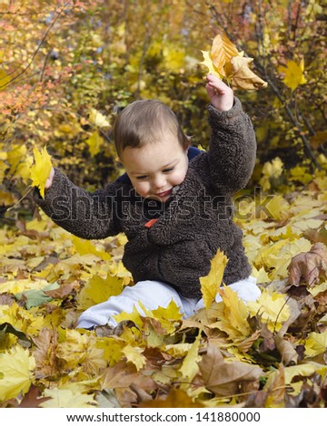 Cute toddler child playing with yellow autumn or fall leaves.