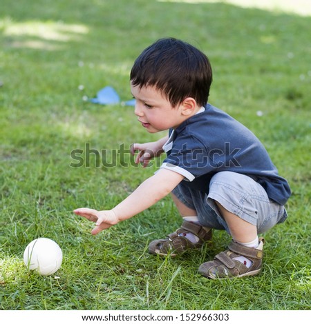A child boy playing with a small  ball on a grass in the garden.