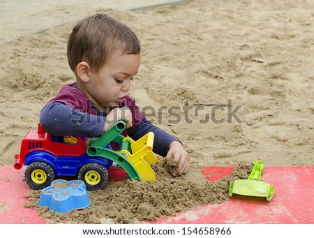 Child playing in sandpit with toy truck car or digger.