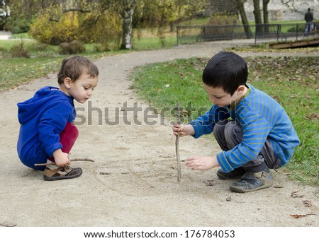 Children drawing into sand on a path in park
