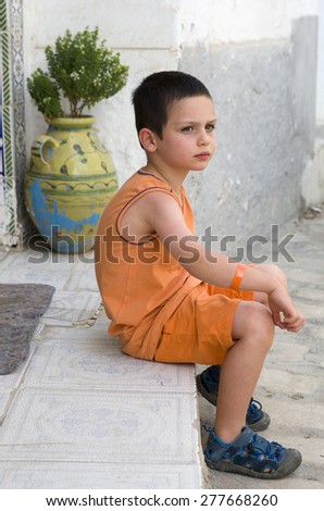 Child boy sitting on street or patio step in summer