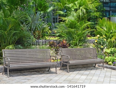 two park benches side by side with tropical plants in the background