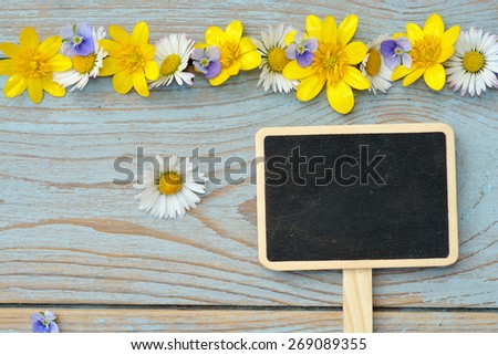 blue grey old wooden background with field flowers, buttercups and daisies with a chalk board