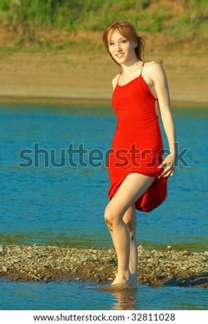 Beautiful girl in a red dress on the river coast. Girl knees a little dirty.