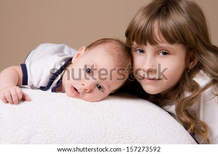 older sister hugging her baby brother on beige background