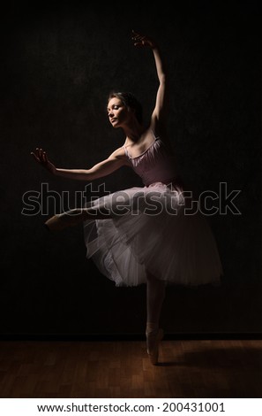 Ballerina in white tutu in dance pose in shadows