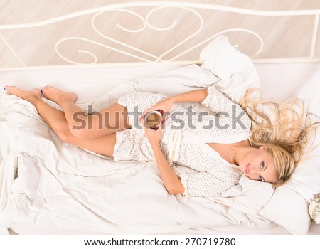 good morning for young attractive blonde woman lying in bed with cup of coffee