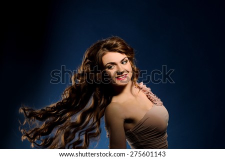 young smiling woman with flying long thick curly hair on dark studio background