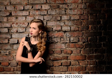young attractive woman with thick braid in black gown on old brick wall background