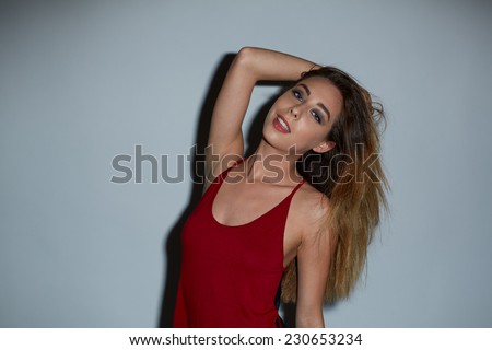 Attractive young woman with long blond hair tossing back her head with her arm raised as she smiles at the camera, studio portrait on grey