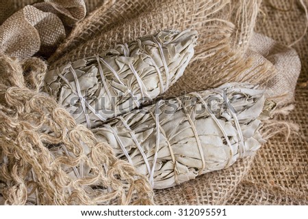Dried white sage bundle wrapped with string surrounded by burlap and natural fibers.