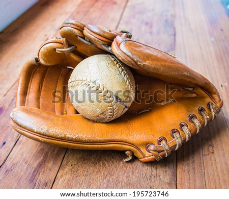 Old worn leather baseball glove and used ball on wood table