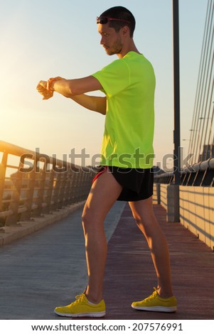 Urban jogger on a big bridge checking his running time.