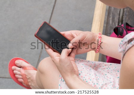 Female typing messages on his smart-phone while sitting on a park bench.