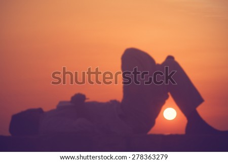 Young poet with crossed legs enjoying loneliness in the sunset time. Focus on the sun.