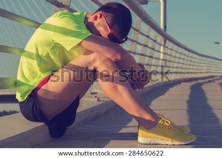 Tired urban jogger making a pause after forcing his body on a big bridge.