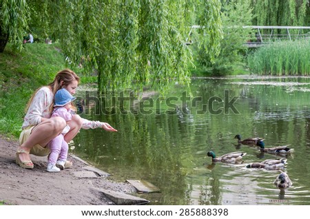 Mom and daughter feeding ducks in a park on the lake