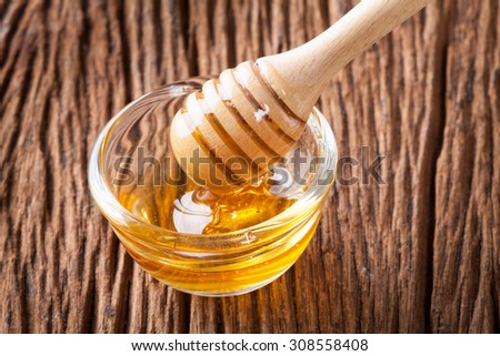 Honey bowl with dipper and flowing honey on the wood table