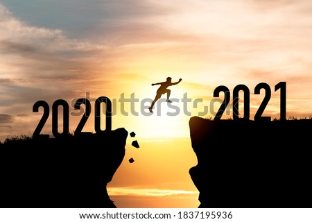 Welcome merry Christmas and happy new year in 2021,Silhouette Man jumping from 2020 cliff to 2021 cliff with cloud sky and sunlight.