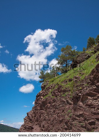 Rocky slope with trees on a background of clouds