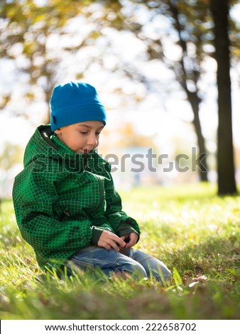 Preschooler with a sad expression on his face sitting on green grass on a blurred background