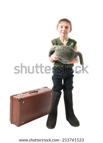 Homeless little boy standing in felt boots next to a suitcase and begs for alms holding in hands hat on a white background