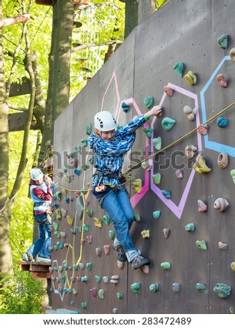 Mother and son in a helmet with safety harness climb the wall on the background of trees and foliage