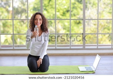 Charming African American holding and drinking bottle of water drink clean clear mineral aqua for healthy and body refreshment after finish yoga excercise. Happy female sitting in living room at home  商業照片 © 