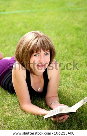 girl reading book outdoors laying on the green grass
