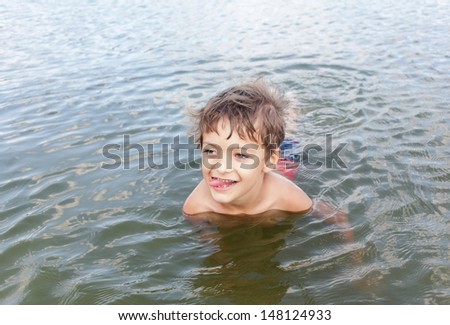 Head of little  kid  boy playing in green  water outdoors on summer day with tongue out