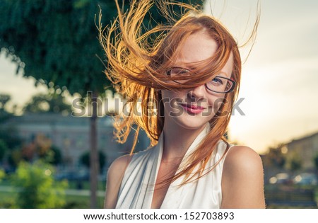 Redhead backlit by the sun. Portrait of cute red haired young woman, outdoors in the park, backlit. Hairs on the wind.