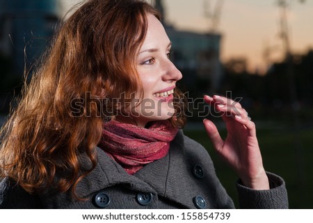 Head and shoulders portrait in profile of the smiling redhead 20s women outdoor in autumn park, weared scarf and coat