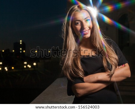 Model smiling. City lights on background and around of the model. Beautiful blond woman alone outdoors at night