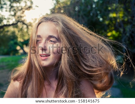closeup shot of long haired women outdoors. She is looking away of camera. Hair is flying