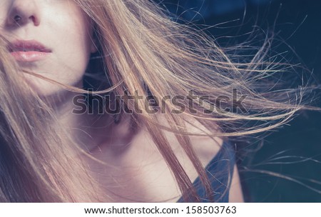 Hair fly by the wind. Very closeup portrait of a half-full face of beautiful young woman on a dark nature background. Outddors shot in the evening time. Toned image.