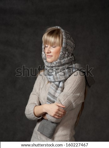 winter fashion shot of a beautiful girl with long curled blonde hair wearing a grey woolen cap and grey sweater