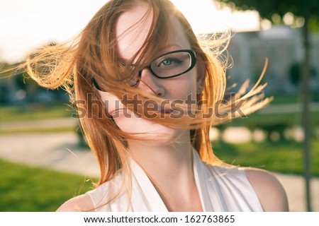 redhead women weared glasses  with hair fly by the wind, outdoors