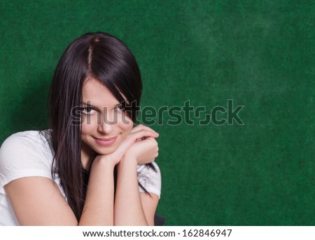 Shy women looking at camera. 20s brunette on green head and shoulders shot