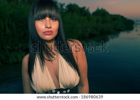 Young pretty brown haired sensual  woman posing against water and green field in summer. Cute smiling girl.