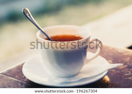White cup of tea on a edge of wooden table in cafe