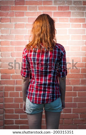 Back side view of a redhead female befor red brick wall