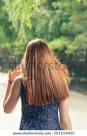 Rear view of a long haired redhead women walking in city park.