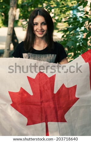 Beautiful patriotic vivacious young woman with the Canada flag held in her outstretched hands standing in the summer sunshine. Canada day