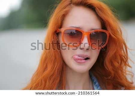 Young red haired women posing in trendy orange sunglasses with her tongue out