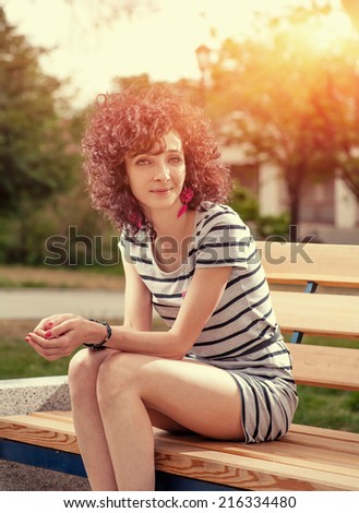 Dark red haired women sitting on the bench in city park in happy state of mind and smiling