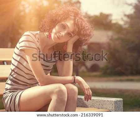 Red haired girl sitting on the bench in city park njoying the warmth of the spring sun