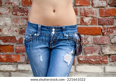 Closeup of the slim belly in jeans against red brick wall